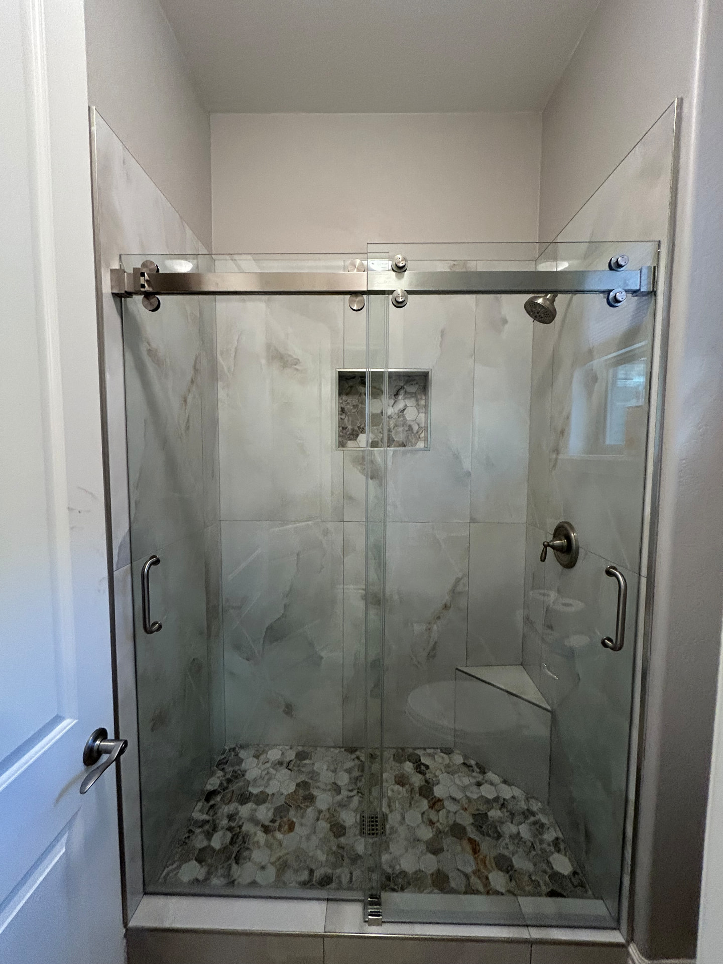 Frameless glass shower enclosure with marble tile